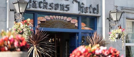 Exterior del hotel Jacksons, con una entrada azul, paneles de vidrio decorativos y arreglos florales colgantes.