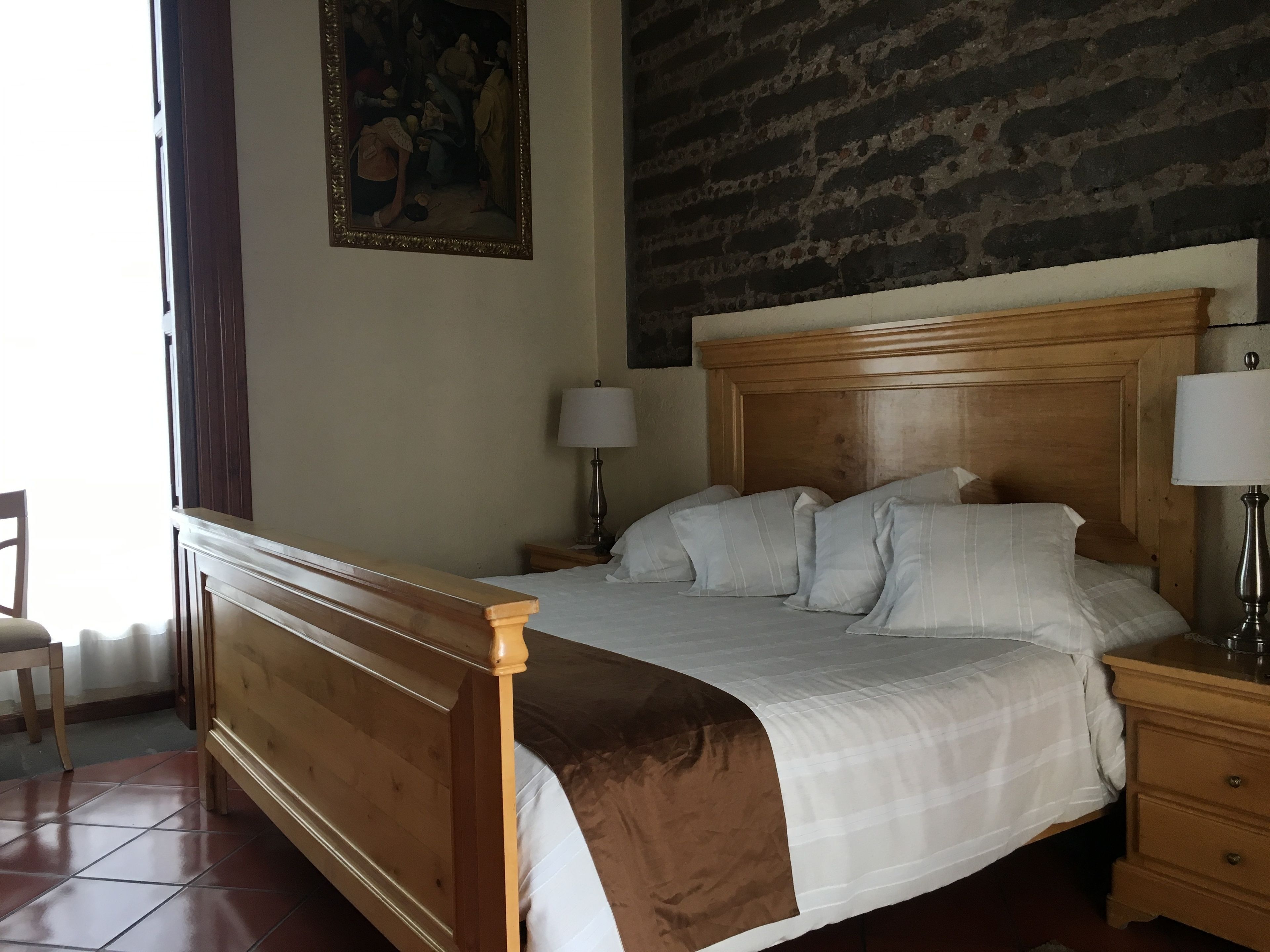 Un dormitorio ordenado con una cama de madera, una mesita de noche con una lámpara y un cuadro en la pared.