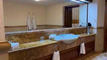 Un baño con un espejo grande, un lavamanos y tocador. Hay toallas colgadas en la pared y un perchero.
