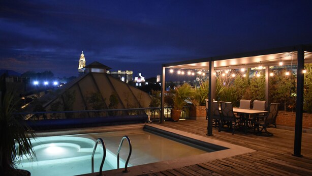 A rooftop pool area with a hot tub, outdoor seating, and a view of a cityscape at night. - Estrella de Belem (San Pedro Cholula)