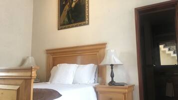 Habitación de hotel con cama de madera, ropa de cama blanca, mesita de noche con lámpara y un cuadro en la pared.
