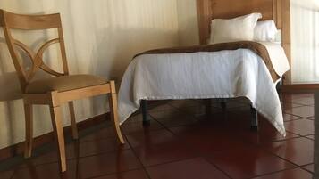 Una habitación con una cama, una silla de madera y suelo de baldosas.
