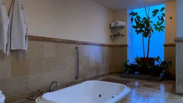 A bathroom with a white bathtub, a towel rack, a handrail, a sink, and a potted plant.