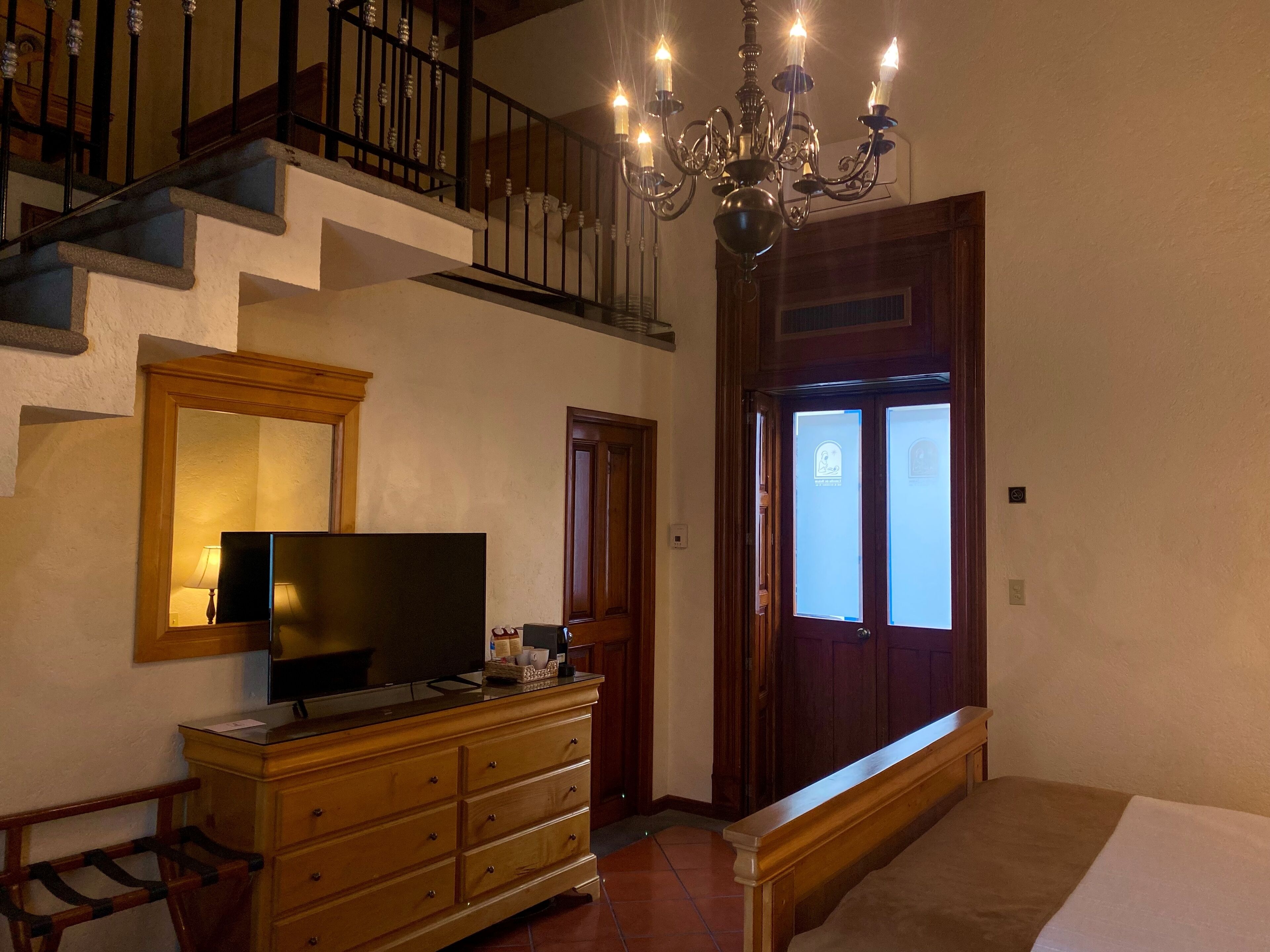 A bedroom with a wooden dresser, a television, a chandelier, and a staircase.