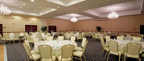 A large banquet hall with round tables and chairs, chandeliers, and a carpeted floor.