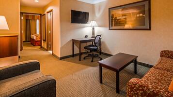A hotel room with a desk, chair, TV, lamp, and a sofa.