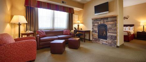 A hotel room with a sofa, armchair, ottoman, fireplace, television, and lamps.