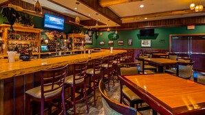A bar area with wooden bar counters, stools, and tables. There are bottles and glasses on the shelves, and a television mounted on the wall. - Best Western Plus Ticonderoga Inn & Suites (Ticonderoga)