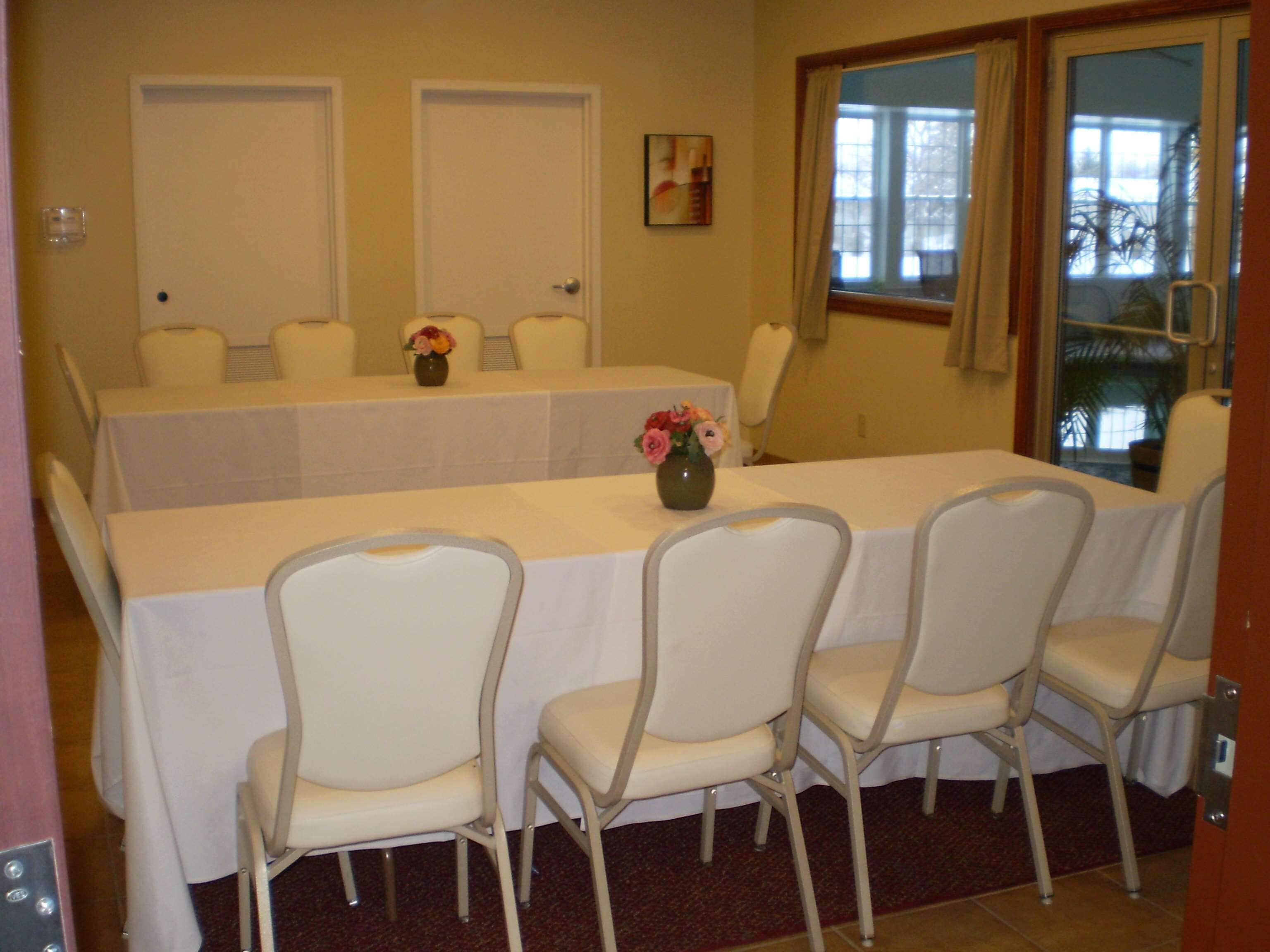 Ein Konferenzraum mit langem Tisch, vier Stühlen, zwei Türen und einem Fenster mit Vorhängen.