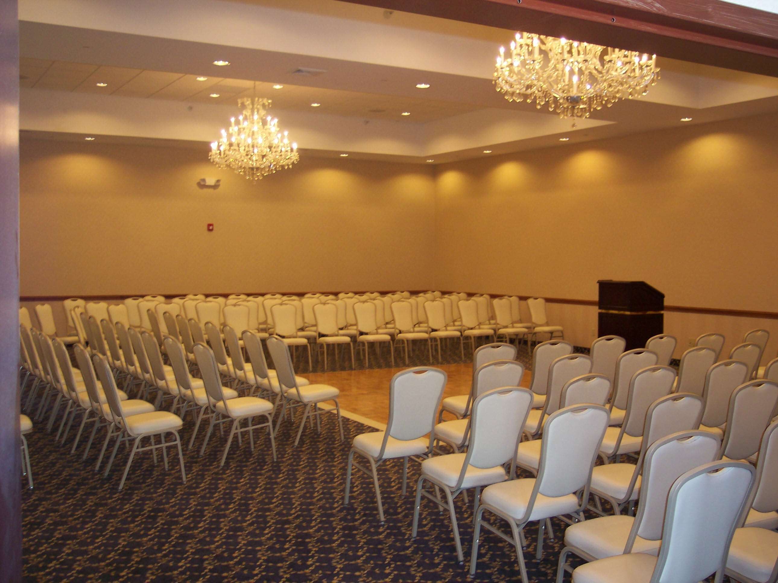 Un salón de conferencias con filas de sillas blancas, piso alfombrado y dos candelabros.