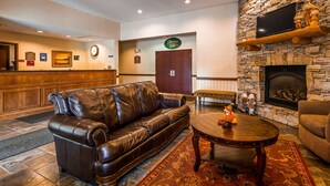 A lobby with a leather sofa, a round coffee table, a stone fireplace, and a reception desk. - Best Western Plus Ticonderoga Inn & Suites (Ticonderoga)