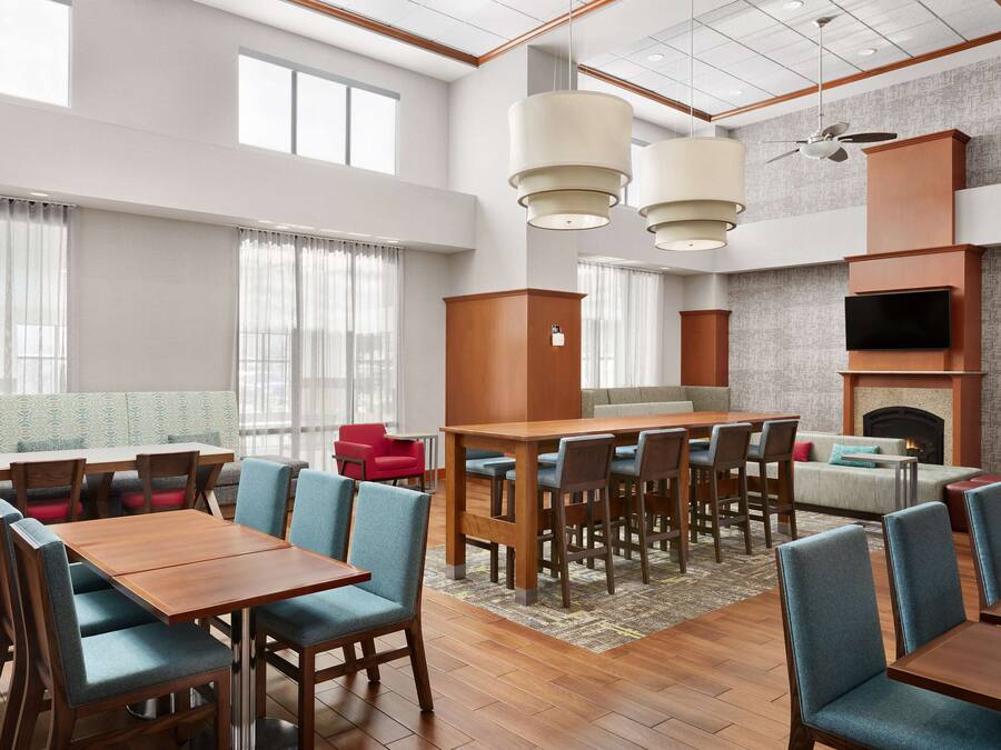 A hotel dining area with wooden tables and blue chairs, a sofa, and a fireplace.