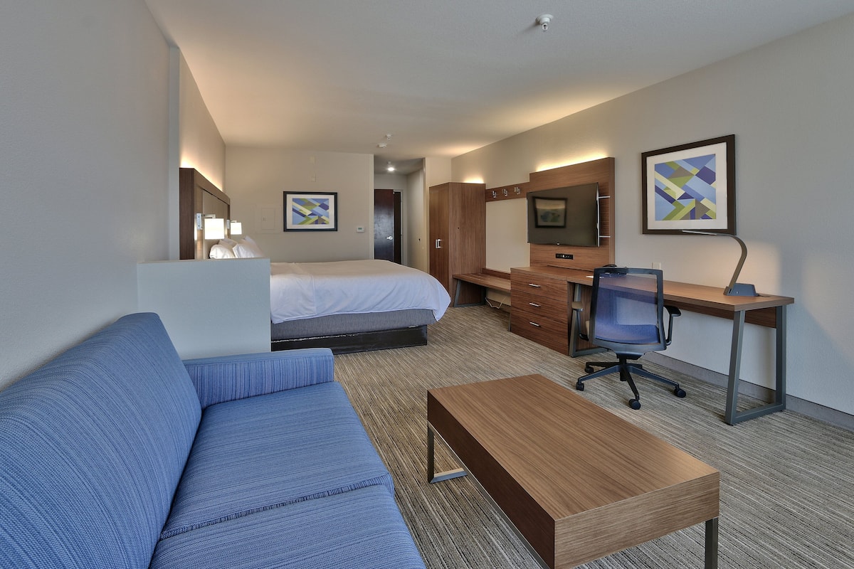 A hotel room with a bed, a blue sofa, a wooden desk, a chair, a TV, and artwork on the walls.