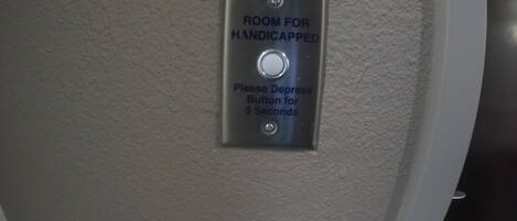 A sign indicating a room for handicapped individuals with a depress button for 5 seconds.