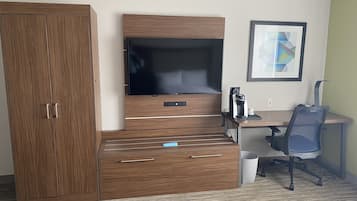 A hotel room with a wooden wardrobe, a flat-screen TV, a desk with a coffee maker, and a framed abstract painting on the wall.