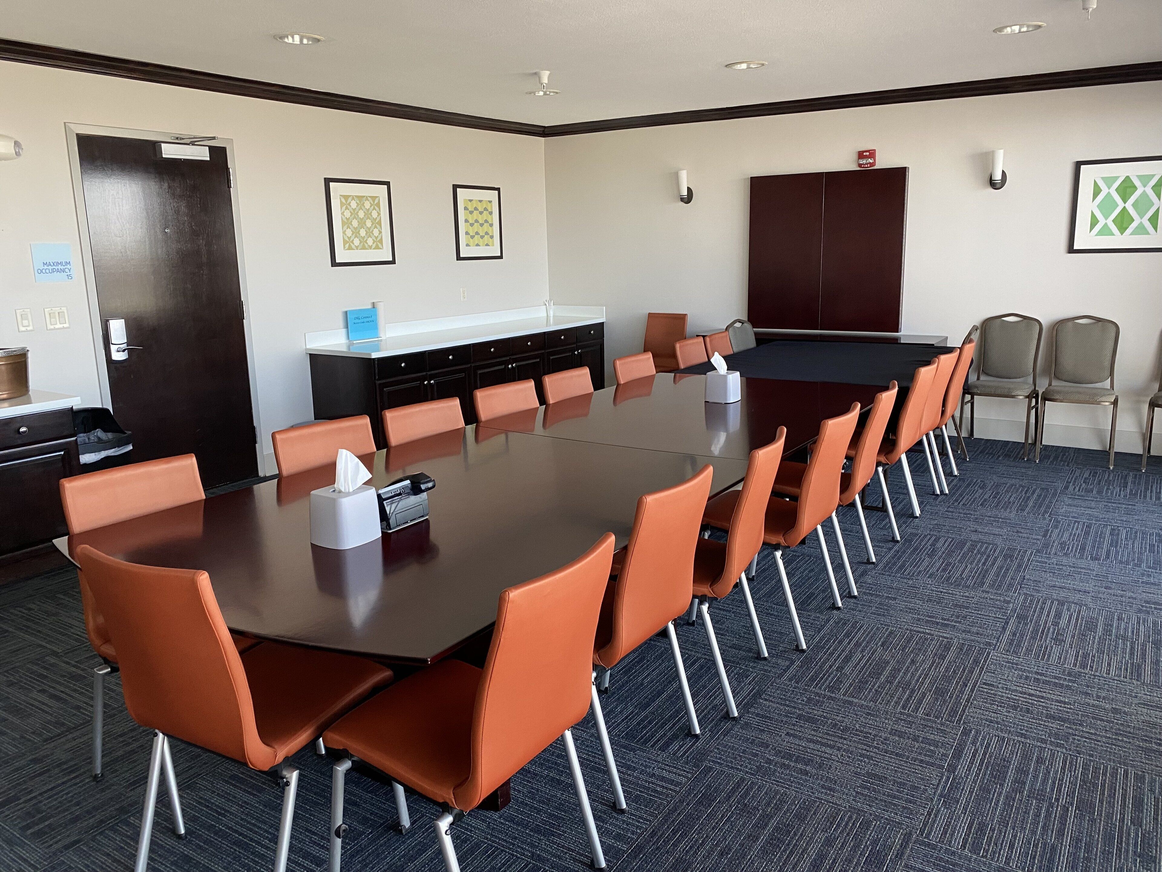 A conference room with a long table, orange chairs, a black conference table, and a dark carpeted floor.
