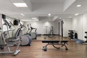 Een moderne fitnessruimte met cardioapparaten, een bank en gewichthefapparatuur.
