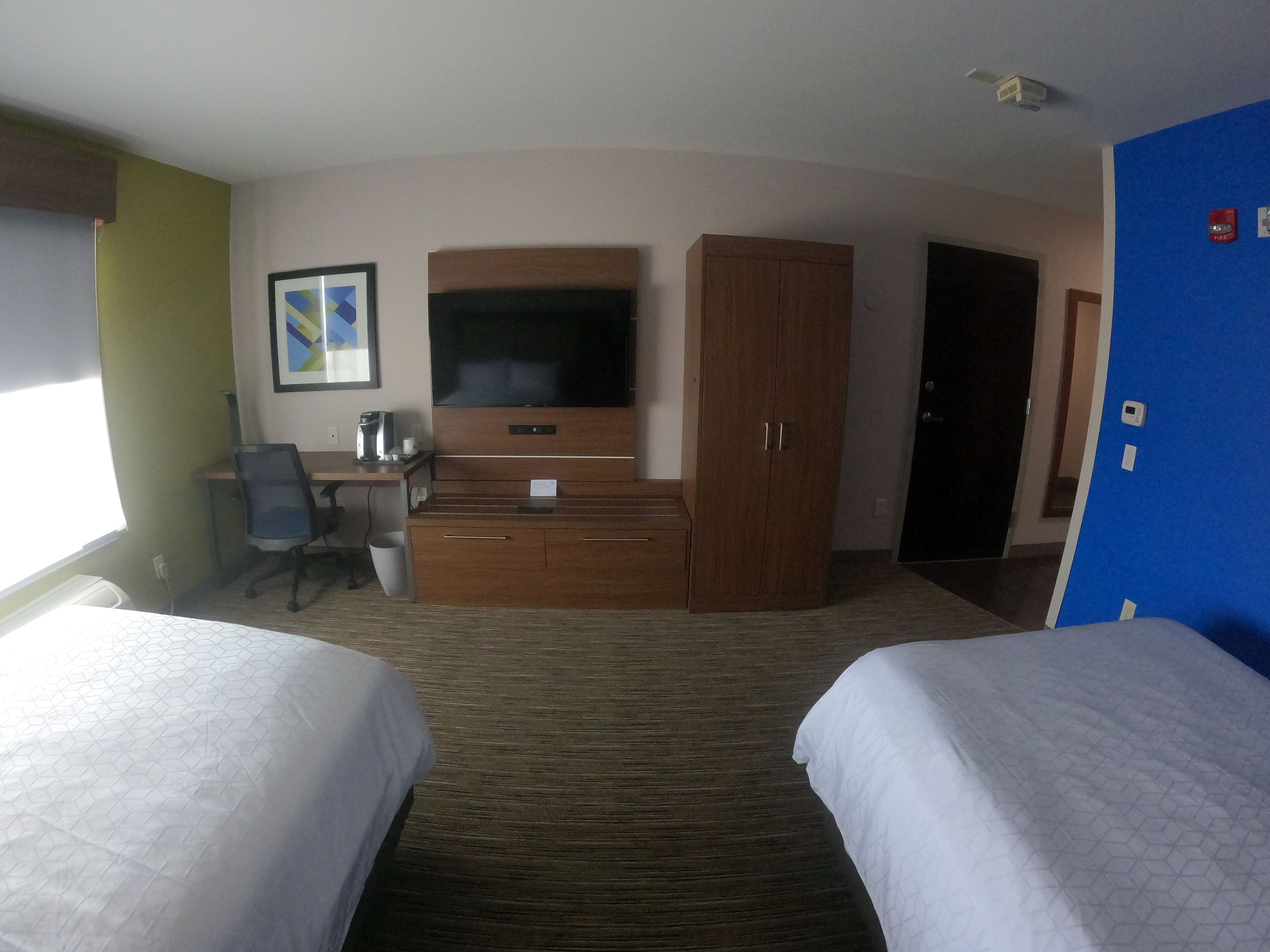 A hotel room with two beds, a desk with a chair, a television, a wardrobe, and a door.