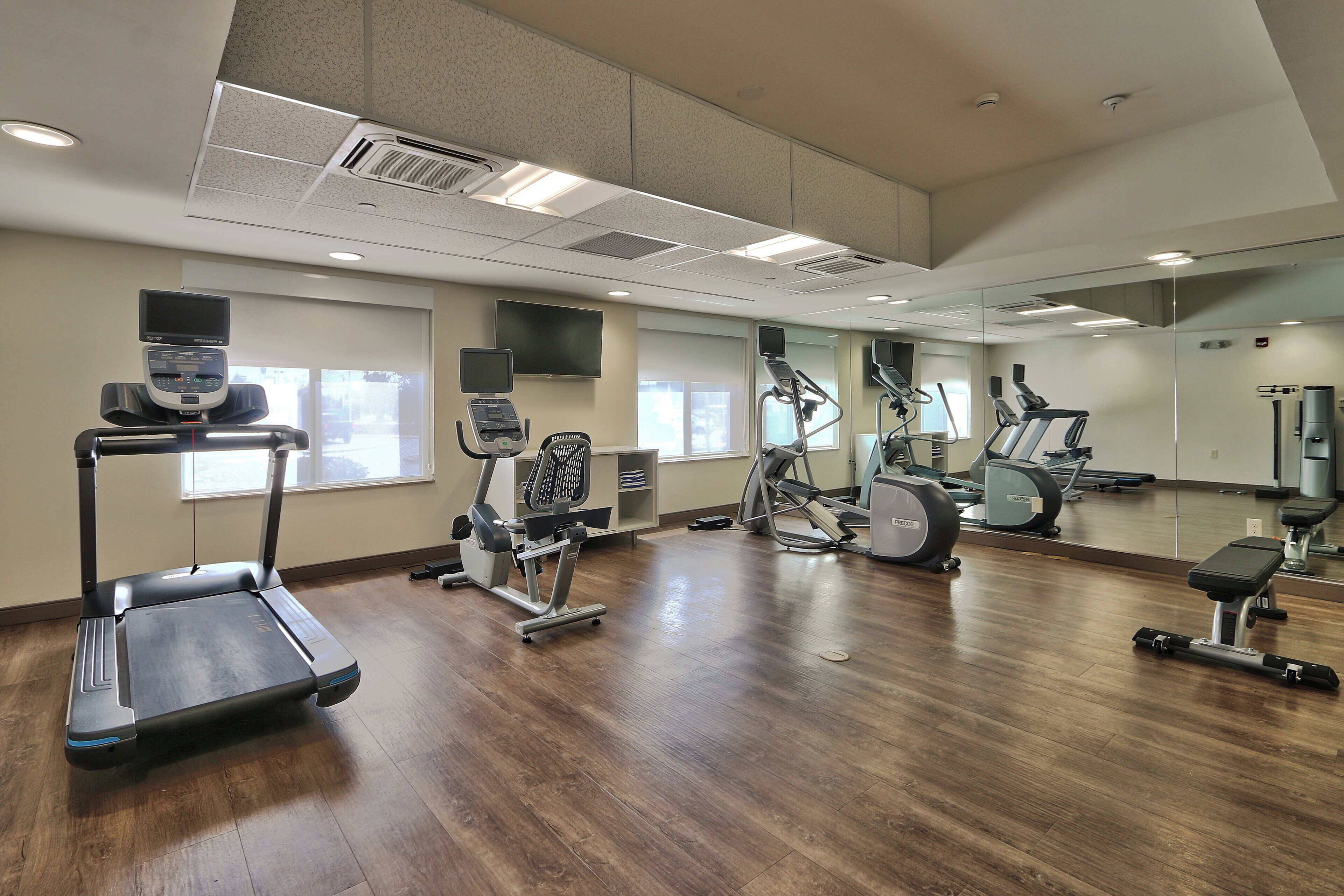 Ein Fitnessstudio mit unterschiedlichen Trainingsgeräten, großen Fenstern und einer Spiegelwand.