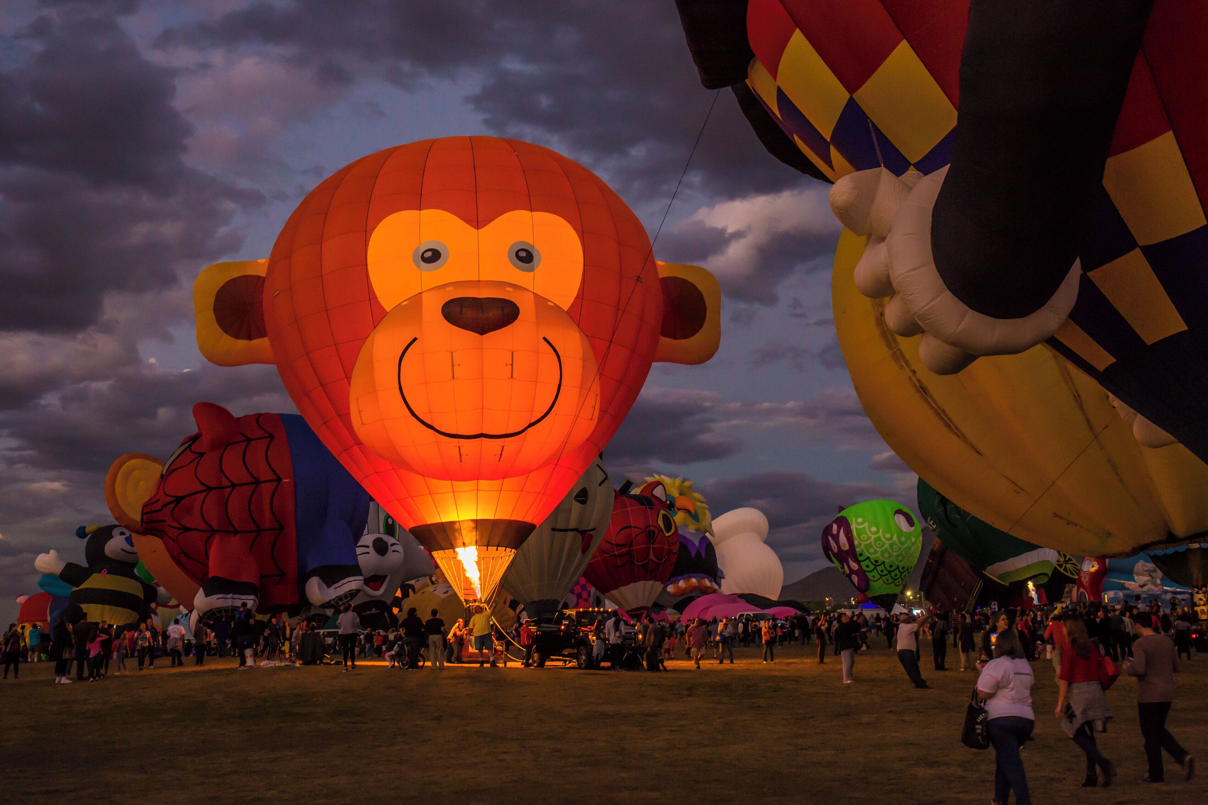 Una multitud numerosa se reunió alrededor de varios globos aerostáticos de colores, incluyendo un globo con forma de oso que destacaba.