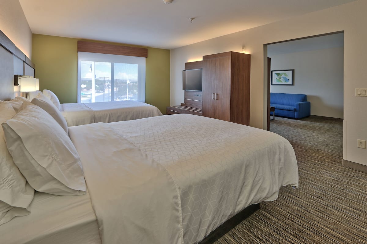 A hotel room with two beds, a TV, a sofa, and a large window.
