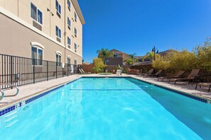 A swimming pool with a tiled edge, surrounded by lounge chairs and a building with multiple windows. - Holiday Inn Express Los Angeles Airport Hawthorne by IHG (Hawthorne)