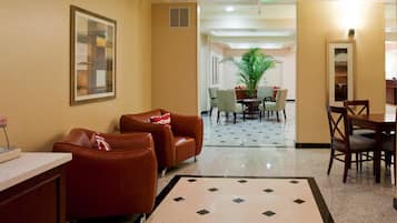 Un vestíbulo de hotel con una zona de estar, una mesa de comedor y una planta grande.