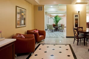Un vestíbulo de hotel con una zona de estar, una mesa de comedor y una planta grande.