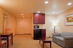A compact hotel room with a kitchenette, a dining area with a table and chairs, a sofa, and a lamp. - Holiday Inn Express Los Angeles Airport Hawthorne by IHG (Hawthorne)