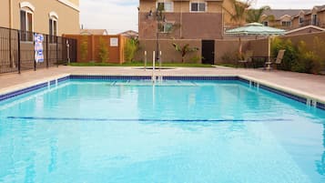 Una piscina cristalina con borde de azulejos, rodeada por una valla y un edificio de techo plano.