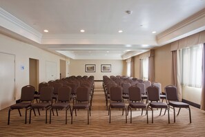 Un salón de conferencias con filas de sillas, piso alfombrado e iluminación empotrada en el techo.
