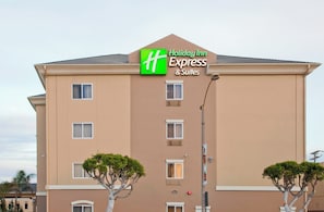 Edificio de Holiday Inn Express & Suites con fachada plana, múltiples ventanas y dos árboles en primer plano.
