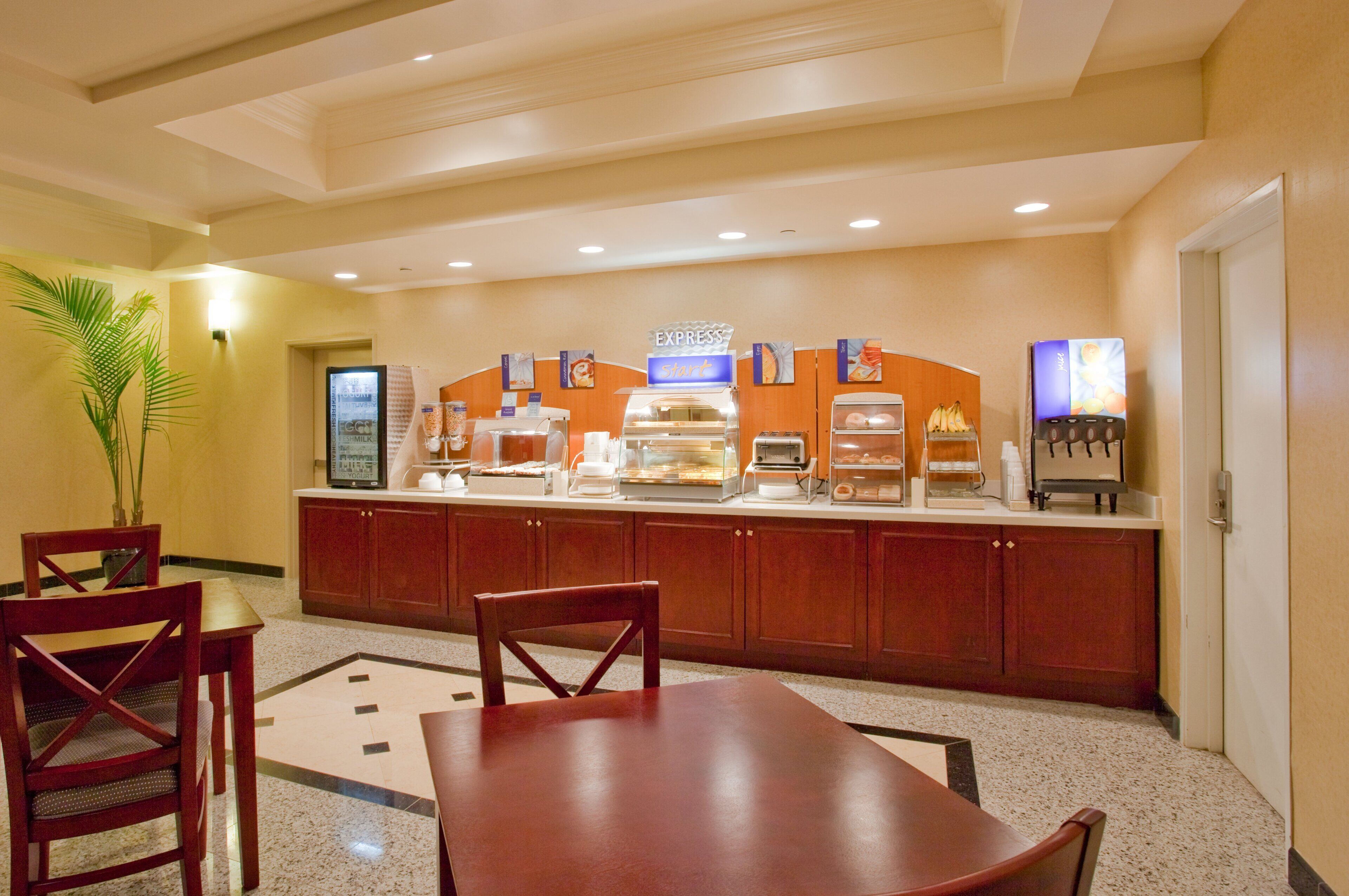 Un área de desayuno de hotel con una barra de buffet, asientos y un refrigerador.