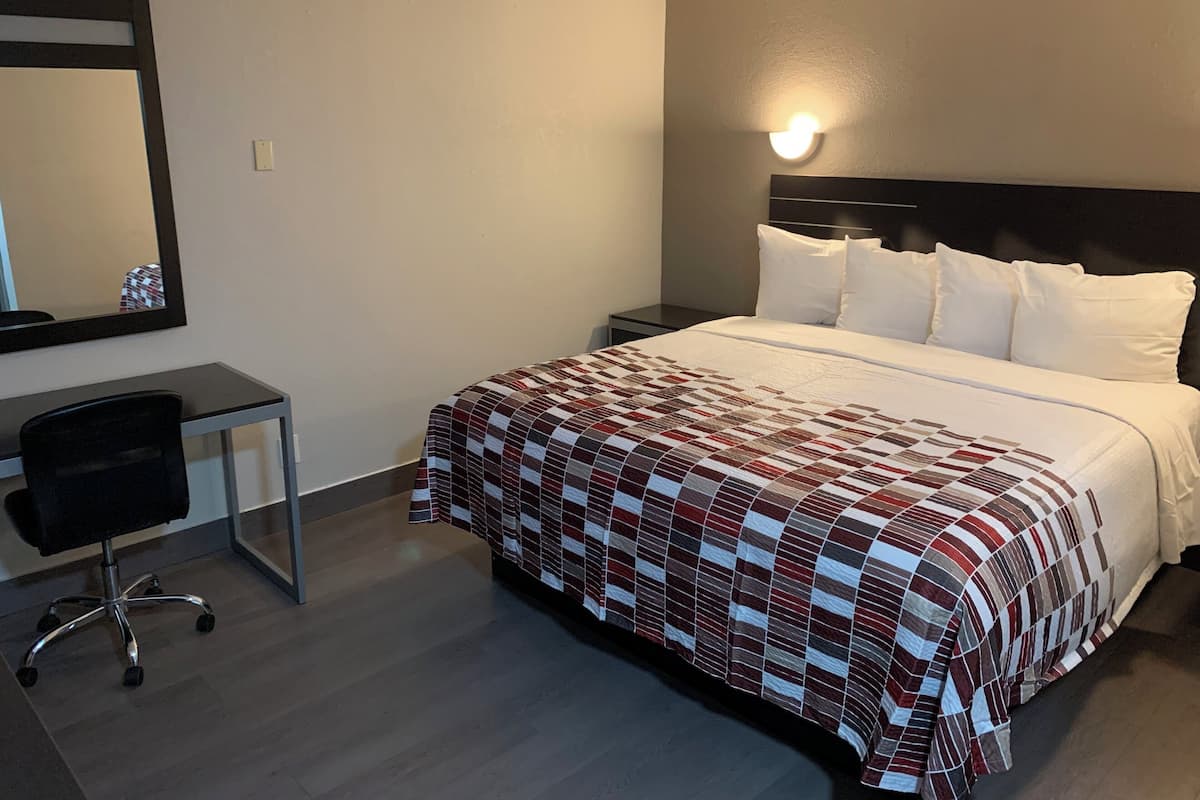 Una habitación de hotel con una cama, un escritorio, una silla y una mesita de noche.