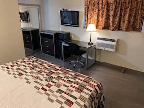 A hotel room with a bed, a desk with a chair, a television, a lamp, and an air conditioning unit. - Red Roof Inn Copiague (Copiague)