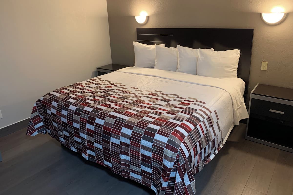 Una cama bien hecha con una colcha a cuadros, dos mesitas de noche con lámparas y un cabecero oscuro.