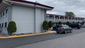 A motel with a red roof and a sign reading "Red Roof Inn." There are several cars parked in front, and a few trees are visible.