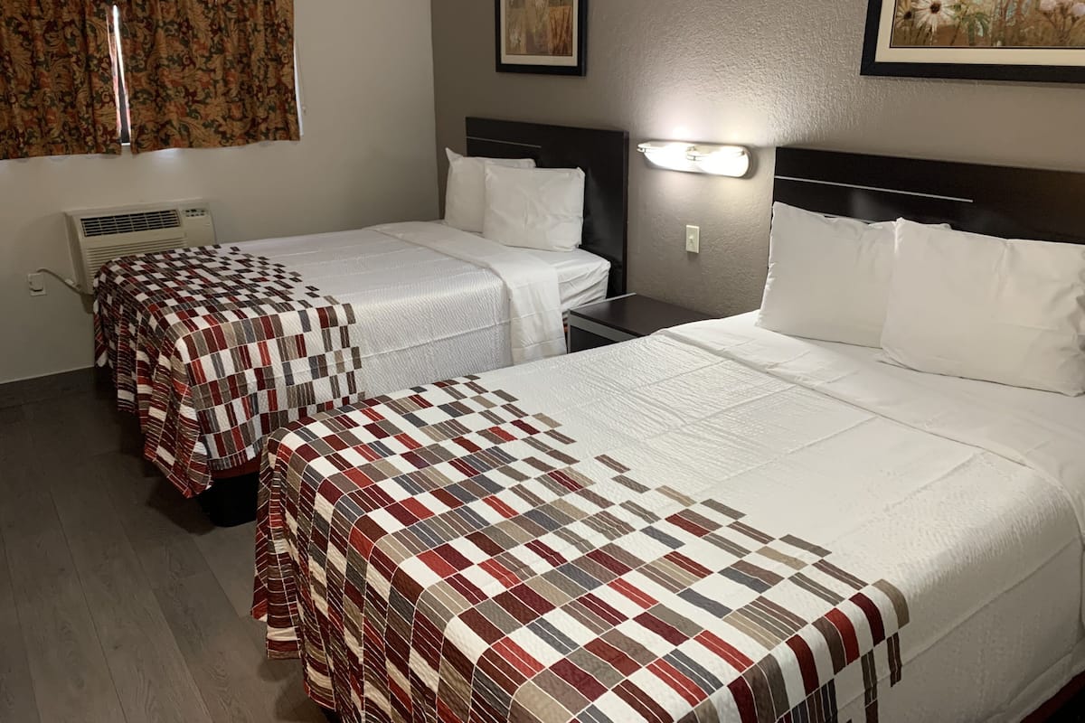 Habitación de hotel con dos camas, cada una con una colcha a cuadros, una mesita de noche con lámpara y un aire acondicionado de pared.