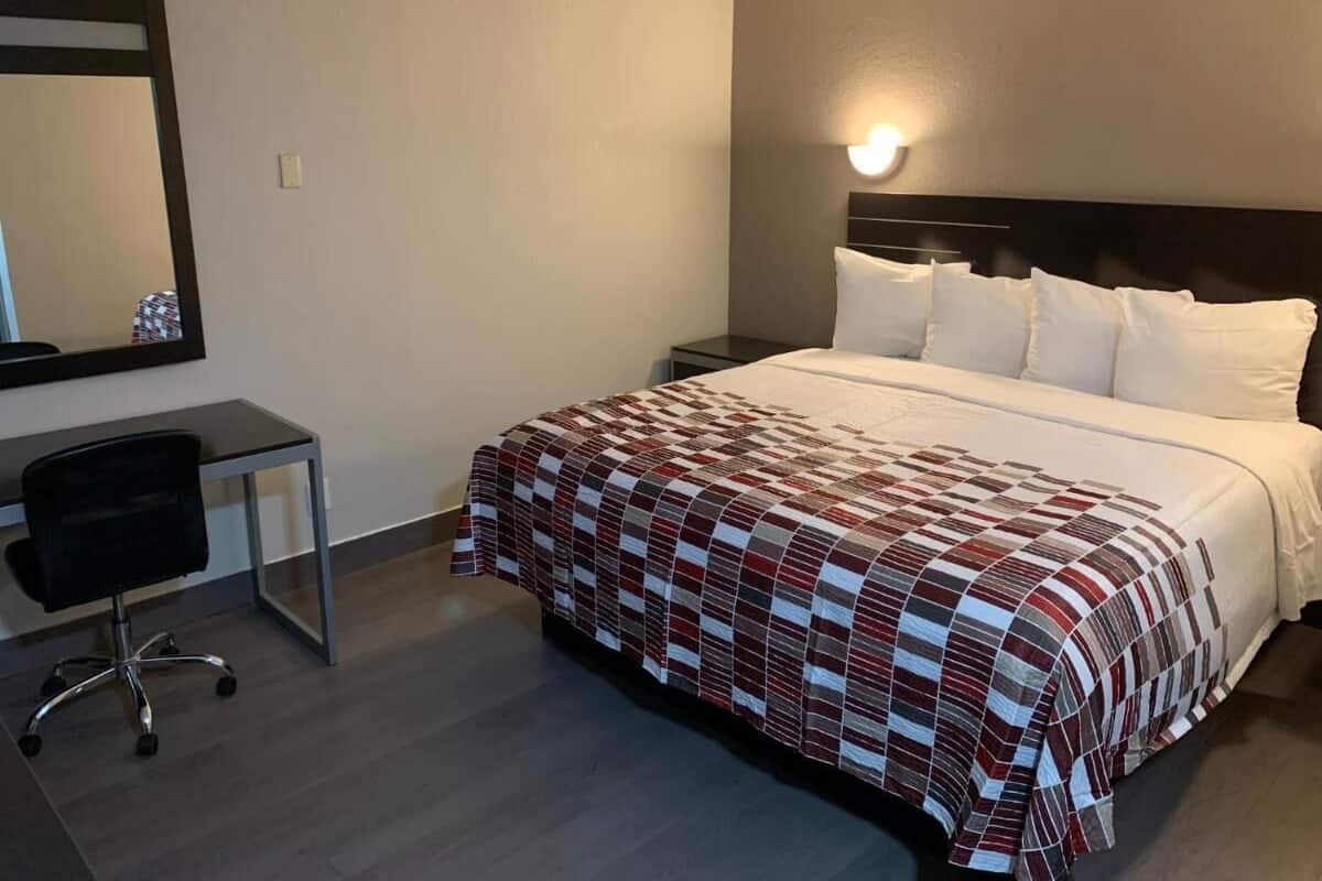 Una habitación de hotel con cama, mesita de noche, silla y espejo en la pared.