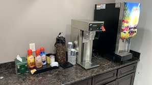 A coffee station with a coffee machine, a juice dispenser, and various coffee and tea products.