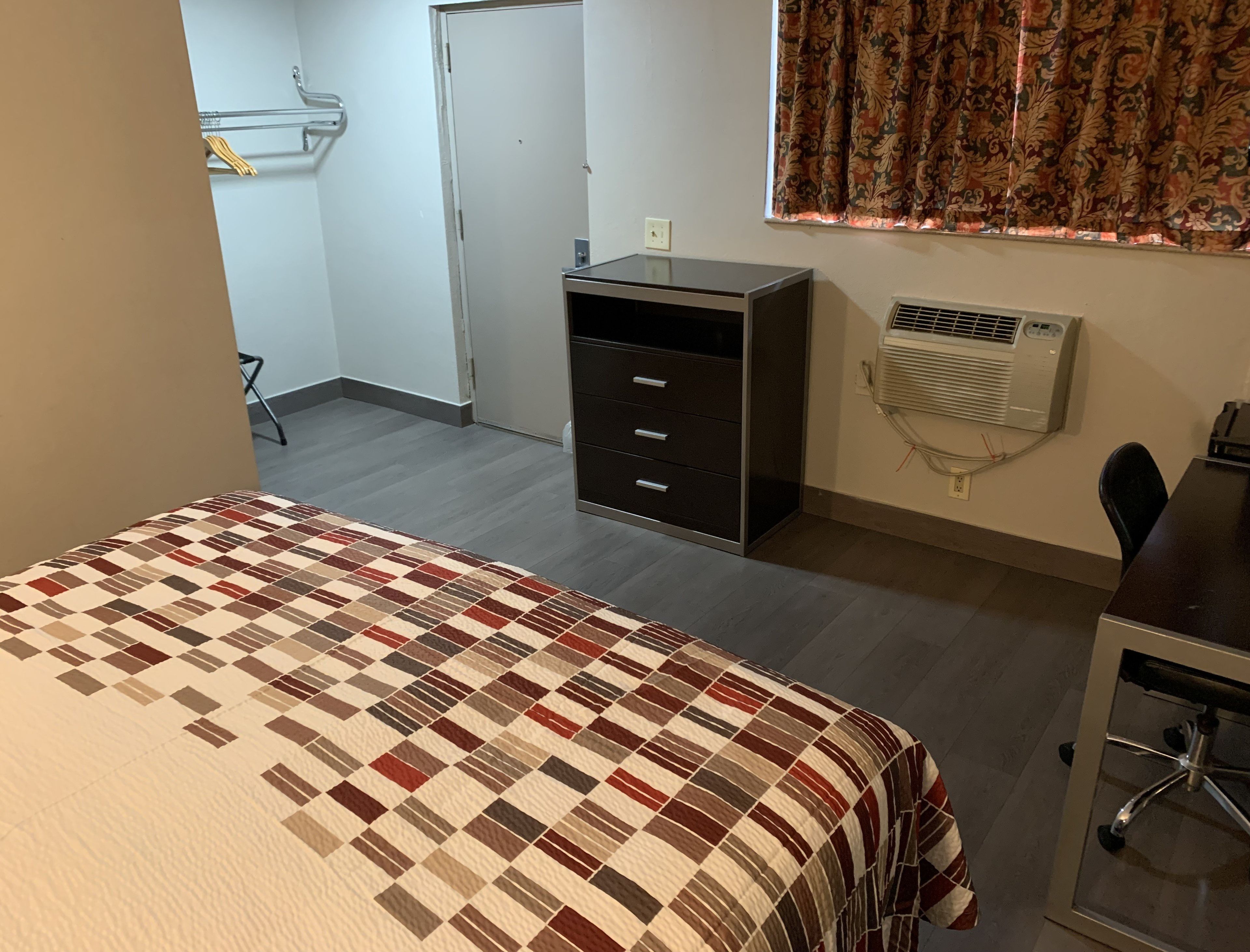 A bedroom with a bed, a desk, a chair, a wardrobe, and an air conditioning unit.