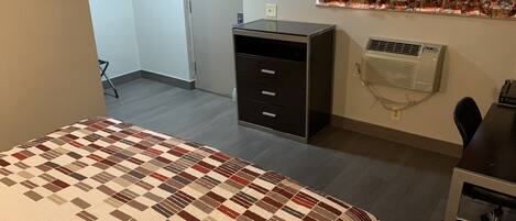 Un dormitorio con cama, escritorio, silla, armario y equipo de aire acondicionado.