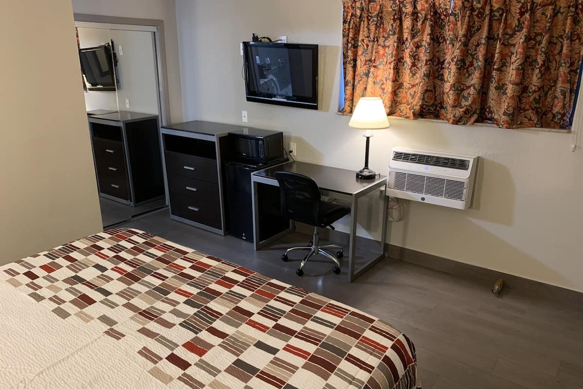 Un dormitorio con cama, escritorio, silla, televisor y aire acondicionado.