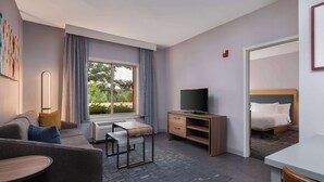 A modern hotel room with a sofa, a small table, a TV, and a bed. - Homewood Suites Medford (Medford)