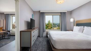 Habitación de hotel con una cama grande, un escritorio con televisor, una ventana con cortinas y vistas al exterior.