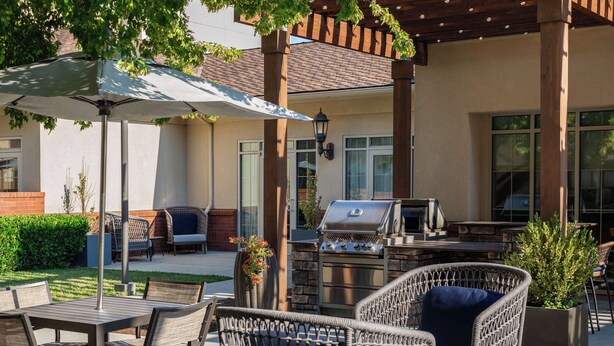An outdoor patio area with a grill, wicker furniture, and a large umbrella. - Homewood Suites Medford (Medford)