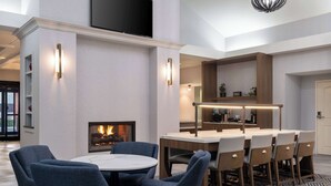 A modern dining area with a round table, blue chairs, and a fireplace. - Homewood Suites Medford (Medford)