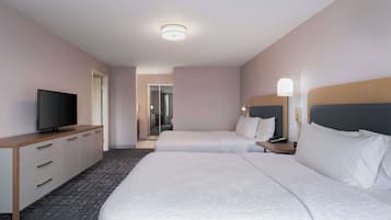 Una habitación de hotel con dos camas, un televisor sobre un aparador de madera y una mesita de noche con lámpara.