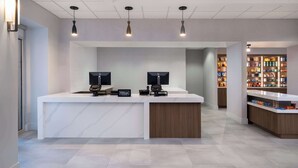 A modern hotel reception area with a marble counter, two monitors, and a minibar. - Homewood Suites Medford (Medford)