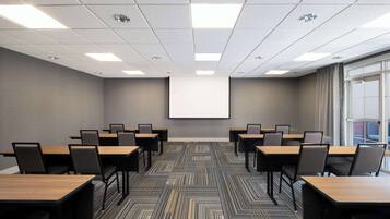 A conference room with a projector screen, multiple tables, and chairs arranged for meetings.